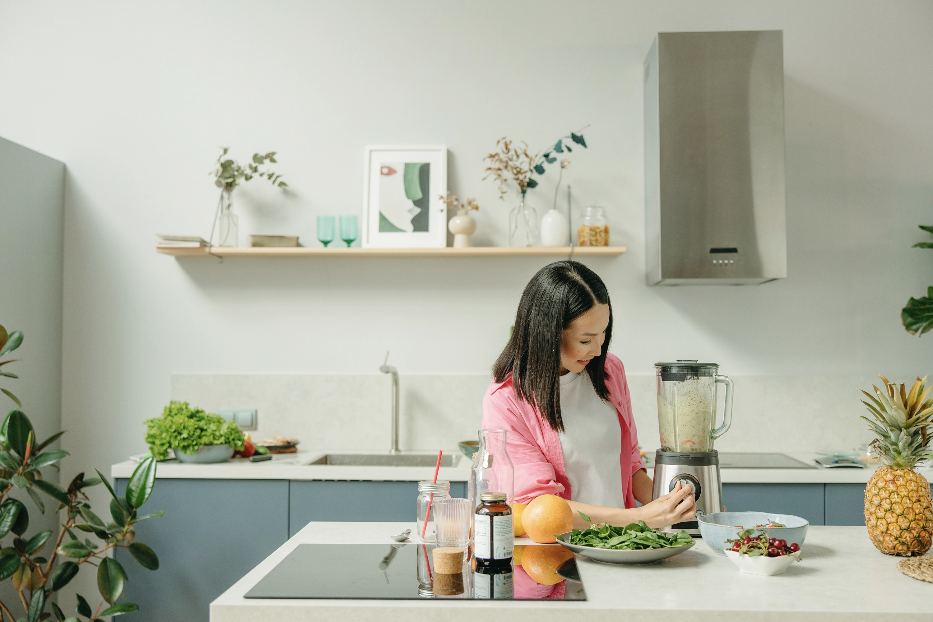 person at a kitchen counter turning on their blender surrounded by 